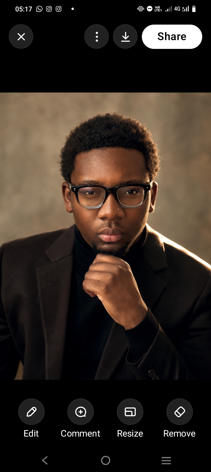 Man in glasses and a black blazer with hand on chin against a warm backdrop