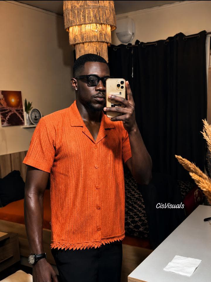 Man in an orange textured shirt taking a mirror selfie in a styled room